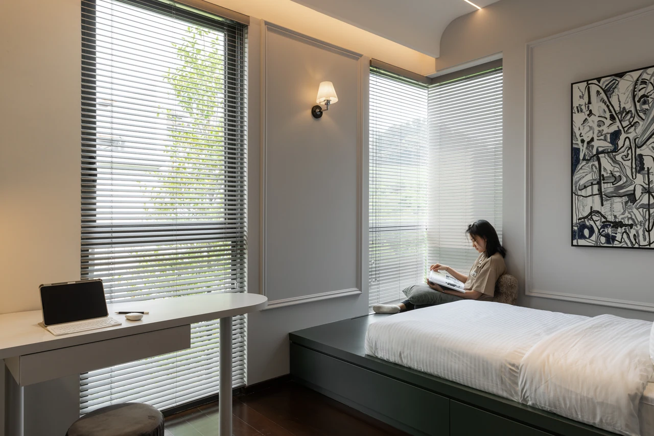 A seated figure by the bedroom window adds an unforced domestic moment.