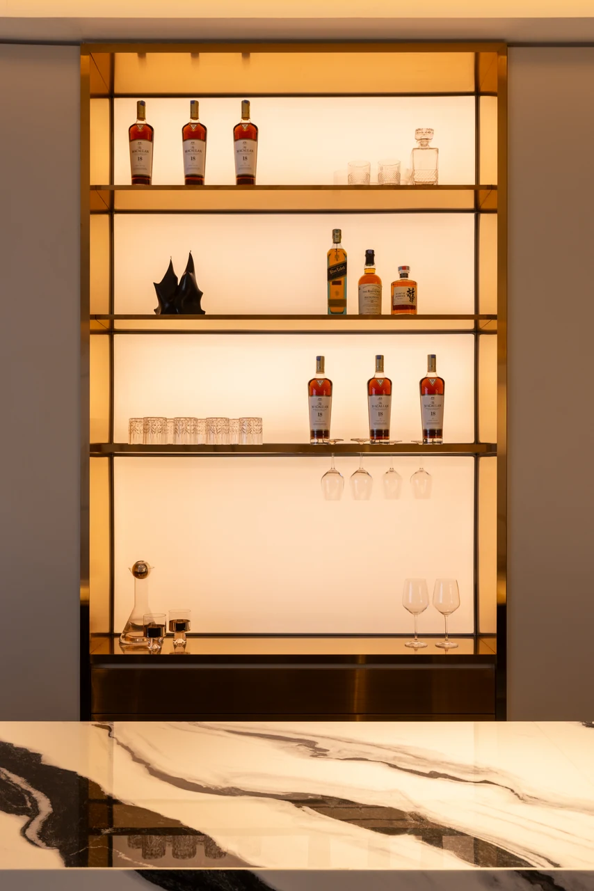 The amber-lit bottle cabinet makes a strong vertical counterpoint to the pale living room.