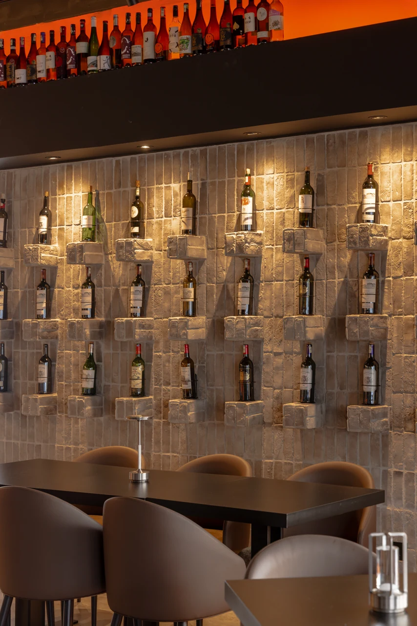 Individual lit bottle niches give the wall treatment a readable close-up.